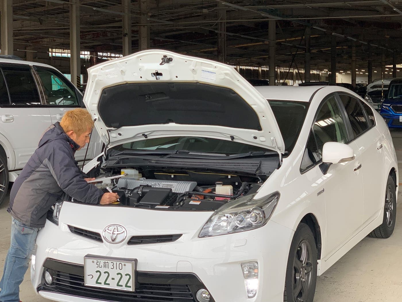 Ito Tadadaka inspecting the engine bay of a white Toyota Prius at auction